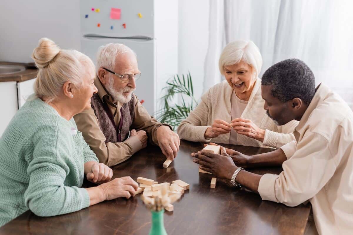 excited senior woman smiling while playing tower wood blocks game with interracial friends